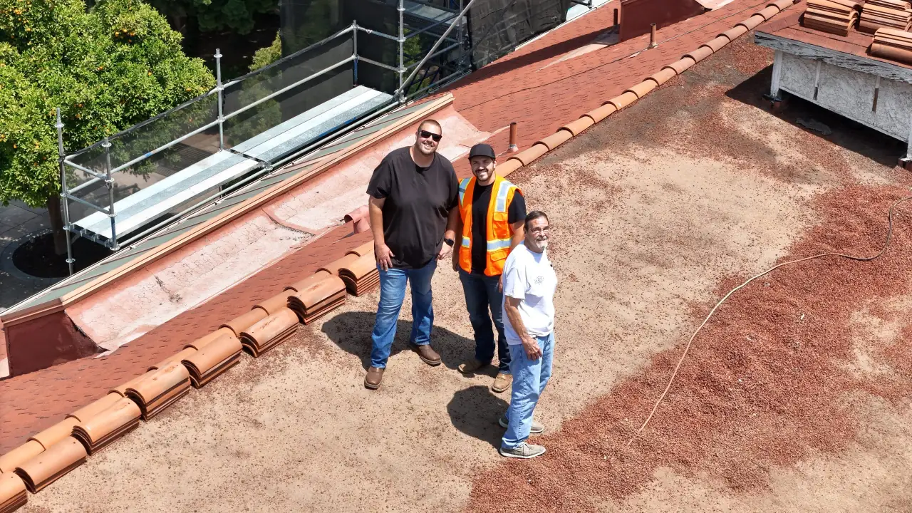 Three people standing on the Mission Inn roof during roofing work